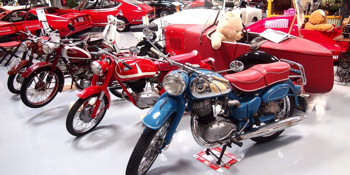 Mehrere Oldtimer-Motorräder und rote Oldtimer sind in einem Ausstellungsraum ausgestellt, in dessen Mitte ein Teddybär in einem roten Beiwagen sitzt.