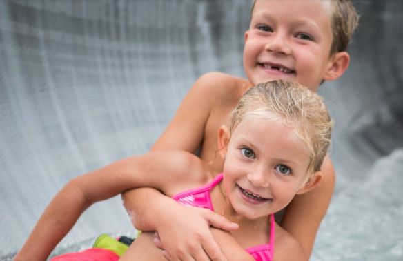 Zwei kleine Kinder lächeln und umarmen sich, während sie eine Wasserrutsche hinunterfahren.