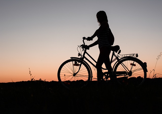 Silhouette einer Person, die bei Sonnenuntergang im Freien neben einem Fahrrad steht, mit einem orangefarbenen und lila Himmel im Hintergrund.
