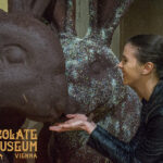 Eine Frau lächelt und posiert mit einer großen Schokoladenhasen-Statue im Schokoladenmuseum Wien.