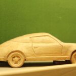 Ein Modellauto aus Holz steht auf einem Regal vor einem grünen Hintergrund.