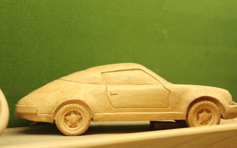 Ein Modellauto aus Holz steht auf einem Regal vor einem grünen Hintergrund.