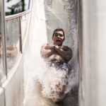 Eine Person rutscht eine Wasserrutsche hinunter, die Arme vor der Brust verschränkt, während das Wasser um ihre Beine spritzt.