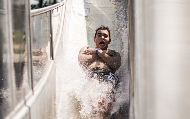 Eine Person rutscht eine Wasserrutsche hinunter, die Arme vor der Brust verschränkt, während das Wasser um ihre Beine spritzt.