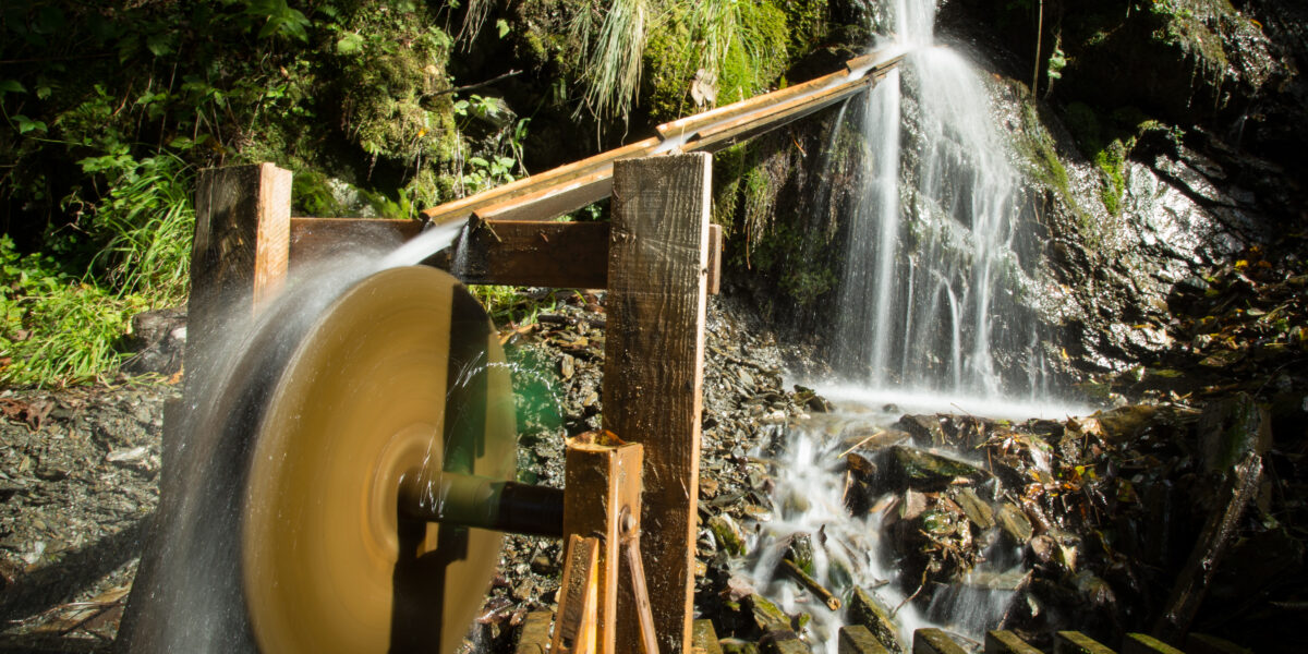 Ein Wasserrad wird durch fließendes Wasser angetrieben, das von einem kleinen Bach in einem Waldgebiet abgeleitet wird.