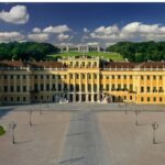 Ein großer gelber Barockpalast mit symmetrischen Flügeln, zwei Springbrunnen davor und einem roten Kreis, der einen Bereich auf der rechten Seite des Gebäudes markiert.