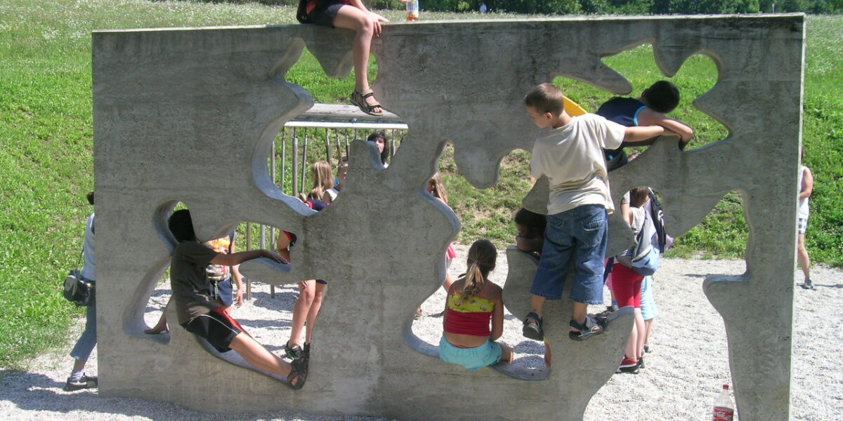 Kinder klettern und spielen auf einer Betonwand mit unregelmäßig geformten Löchern auf einem Spielplatz im Freien.