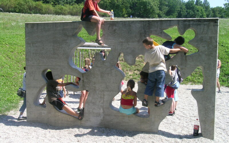 Kinder klettern und spielen auf einer Betonwand mit unregelmäßig geformten Löchern auf einem Spielplatz im Freien.
