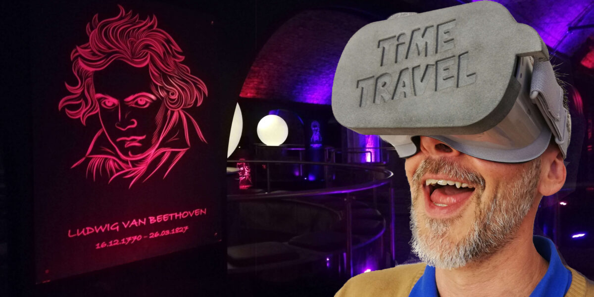 Ein Mann, der ein Virtual-Reality-Headset mit der Aufschrift "ZEITREISE" trägt, steht in einem neonbeleuchteten Raum mit einem leuchtenden Beethoven-Porträt an der Wand.