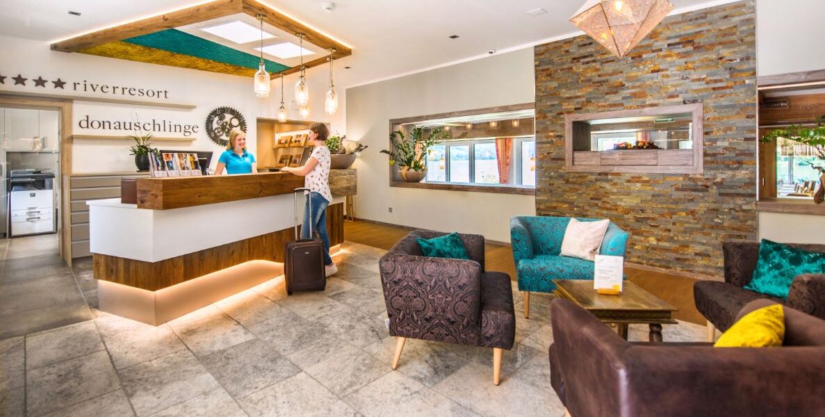 Ein Gast meldet sich an der Rezeption einer modernen Hotellobby mit Sitzecke, Steinakzenten und warmer Beleuchtung.