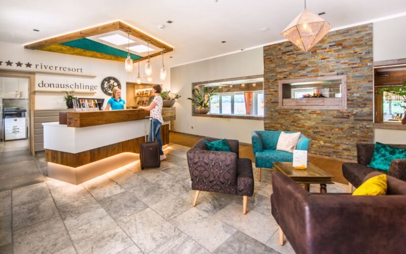 Ein Gast meldet sich an der Rezeption einer modernen Hotellobby mit Sitzecke, Steinakzenten und warmer Beleuchtung.