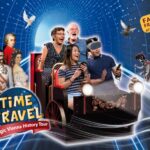 Vier Personen, zwei davon mit Virtual-Reality-Headsets, fahren in einem Themenfahrzeug durch einen digitalen Tunnel mit historischen Figuren und Tauben und werben für die "Time Travel: Magische Wiener Geschichte Tour".