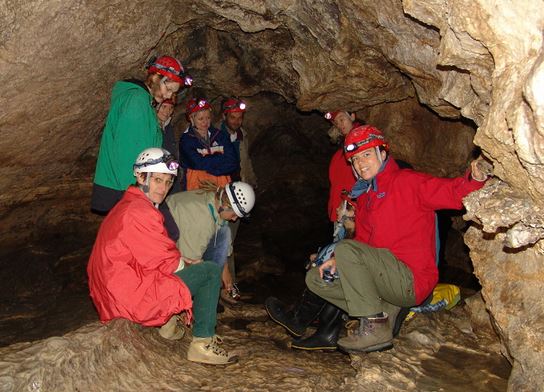 Eine Gruppe von Menschen mit Helmen und Stirnlampen sitzt und kniet in einer Felshöhle und posiert für ein Foto.