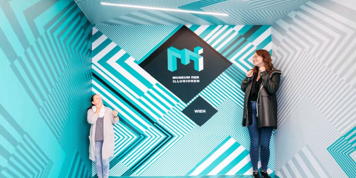 Zwei Personen stehen in einem verzerrten Raum im Museum der Illusionen in Wien, der aufgrund der optischen Täuschung unterschiedlich groß erscheint.