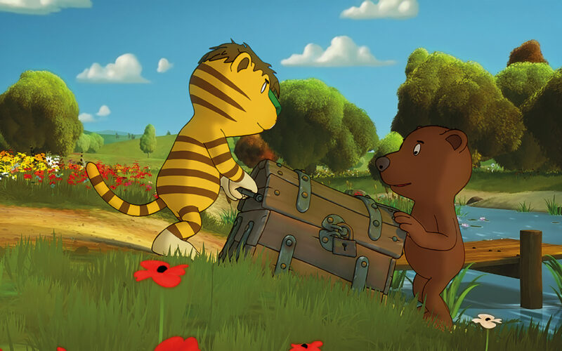 Ein animierter Tiger und ein Bär tragen eine große Truhe neben einem Bach in einer grasbewachsenen, blumenreichen Landschaft mit Bäumen im Hintergrund.