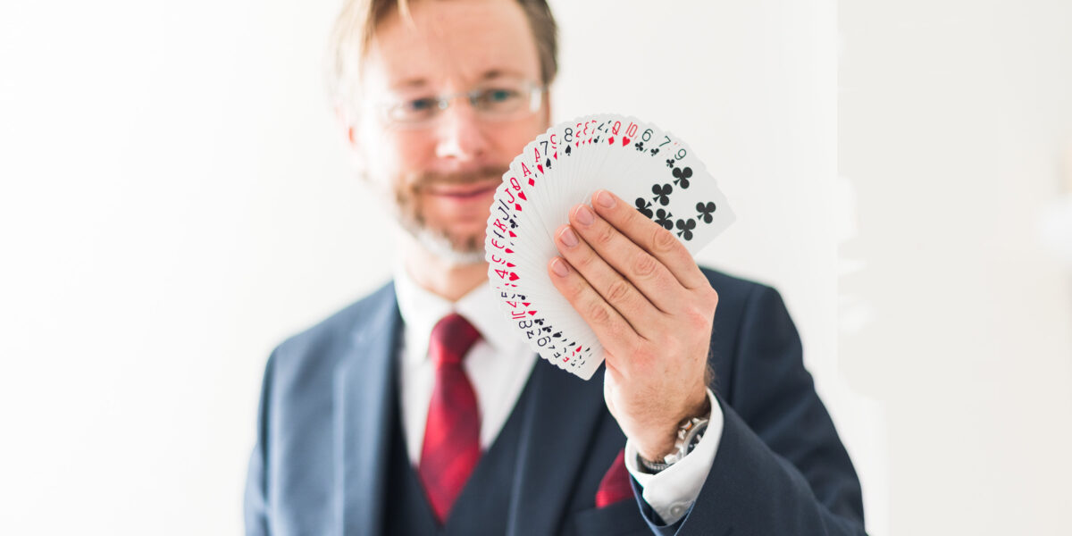 Ein Mann im Anzug und mit roter Krawatte hält ein aufgefächertes Spielkartenset in die Kamera.