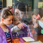 Eine Frau und zwei Kinder sehen sich eine Museumsausstellung mit einem Schiffsmodell hinter Glas genau an und lesen eine Informationstafel.