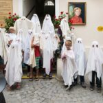 Eine Gruppe von Kindern und Erwachsenen, die als Gespenster mit weißen Tüchern verkleidet sind, posieren gemeinsam in einem Innenhof.