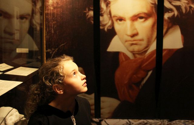 Ein kleines Kind blickt zu einem großen Porträt von Ludwig van Beethoven an der Wand eines Museums auf.
