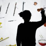 Silhouette einer Person, die eine Hand vor einem Bildschirm hebt, auf dem Abbildungen verschiedener Musikinstrumente zu sehen sind.