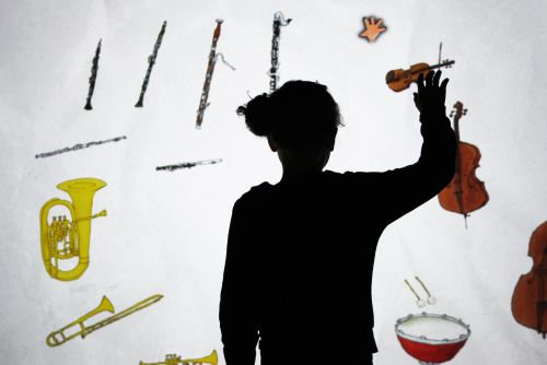 Silhouette einer Person, die eine Hand vor einem Bildschirm hebt, auf dem Abbildungen verschiedener Musikinstrumente zu sehen sind.