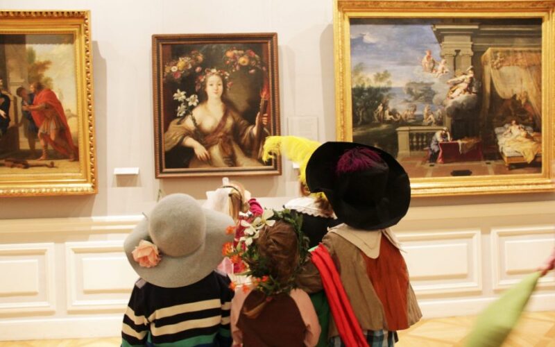 Eine Gruppe von Kindern in Kostümen steht vor gerahmten Gemälden in einem Kunstmuseum und betrachtet die Kunstwerke.