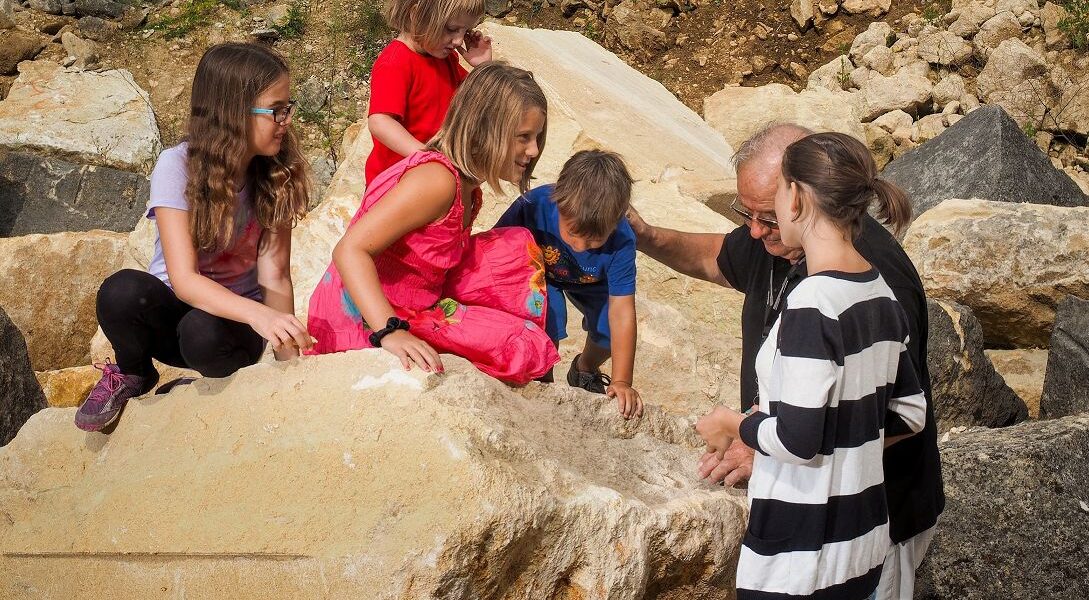 Eine Gruppe von Kindern und zwei Erwachsenen versammelt sich auf einem großen Felsen, wobei die Kinder klettern und die Erwachsenen ihnen dabei helfen.