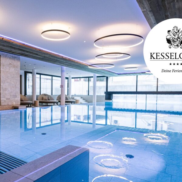 Hallenbadbereich mit moderner Beleuchtung, Liegestühlen und großen Fenstern; das Logo des Hotels Kesselgrub" und der Text WILLKOMMEN" sind auf dem Bild zu sehen.