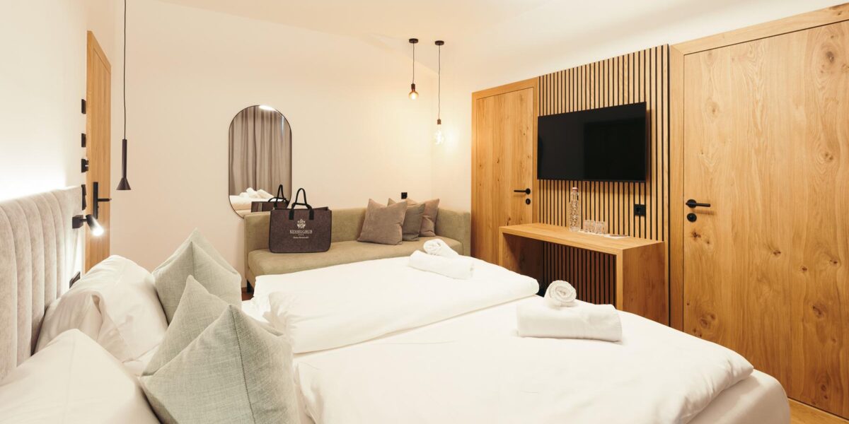 Modernes Hotelzimmer mit zwei sauber gemachten Einzelbetten, einem Sofa, einem an der Wand montierten Fernseher, Holzmöbeln und gedämpfter Umgebungsbeleuchtung.