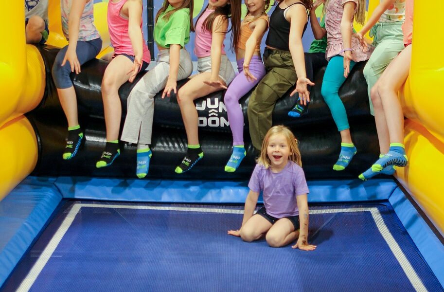 Eine Gruppe von Kindern posiert auf dem Rand eines aufblasbaren Trampolins, wobei ein Kind auf der Matte davor sitzt.