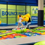 Drei Kinder spielen mit großen gelben Polsterstäben auf einer aufblasbaren Plattform im JUMP DOME Salzburg, dem aufregenden Indoor-Trampolinpark.
