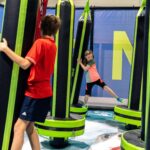 Zwei Kinder spielen auf einem weichen Hindernisparcours im Indoor-Aktivitätszentrum JUMP DOME Salzburg und klammern sich an großen gepolsterten Säulen fest, um das Gleichgewicht zu halten.
