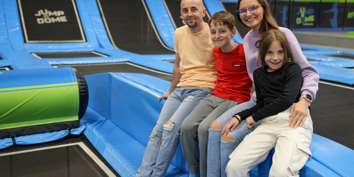 Eine vierköpfige Familie sitzt gemeinsam auf dem gepolsterten Rand des JUMP DOME Klagenfurt und lächelt in die Kamera.