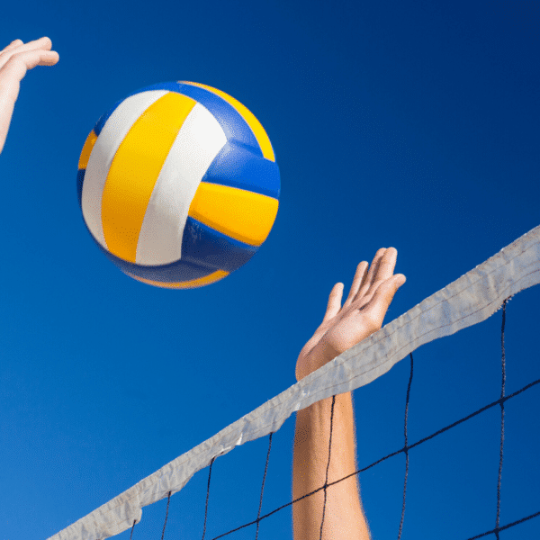 Ein Volleyball schwebt in der Luft über dem Netz, während zwei Spieler vor einem klaren blauen Himmel danach greifen.