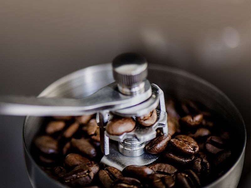 Nahaufnahme von Kaffeebohnen in einer manuellen Kaffeemühle mit einem Metallgriff, bereit zum Mahlen.