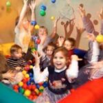 Eine Gruppe von Kindern spielt mit bunten Plastikbällen in einer Ballgrube. Einige werfen die Bälle in die Luft, andere lächeln in die Kamera.