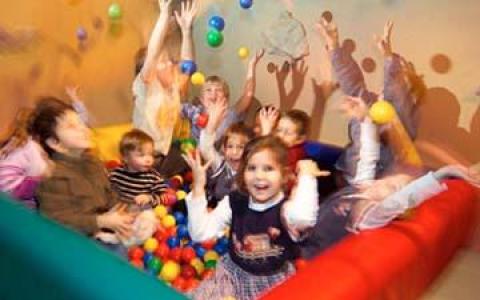 Eine Gruppe von Kindern spielt mit bunten Plastikbällen in einer Ballgrube. Einige werfen die Bälle in die Luft, andere lächeln in die Kamera.