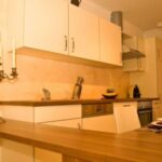 Moderne Küche mit hellen Schränken, einer Arbeitsplatte aus Holz, Einbaugeräten, einem Kandelaber und einer Essecke mit Tellern und Weingläsern.