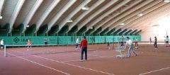 In einer großen Tennishalle mit einem gewölbten Dach wird auf mehreren Plätzen Tennis gespielt und unterrichtet.