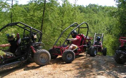 Drei Personen mit Helmen fahren auf einem unbefestigten Weg, der von grünen Bäumen und Pflanzen umgeben ist, Go-Karts.