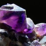 Nahaufnahme einer Gruppe violetter Amethystkristalle, die scharfe Kanten und durchscheinende Oberflächen vor einem dunklen Hintergrund zeigt.