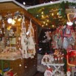 Zwei hölzerne Marktstände, die mit Weihnachtsschmuck und Lichtern geschmückt sind, bieten verschiedene Weihnachtsartikel und Geschenke an, während in der Szene sanft der Schnee fällt.