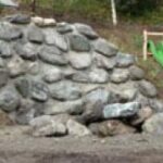 Neben einer kleinen, grünen Plastikrutsche auf dem Spielplatz liegt ein Haufen großer, unebener Felsen auf der Erde.