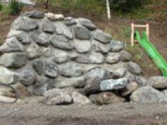 Neben einer kleinen, grünen Plastikrutsche auf dem Spielplatz liegt ein Haufen großer, unebener Felsen auf der Erde.