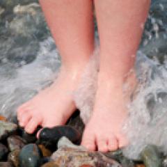 Nackte Füße, die auf nassen Kieselsteinen stehen, während das Meerwasser um sie herum plätschert.