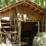 Eine rustikale Holzhütte mit gestapeltem Brennholz, einem montierten Rinderschädel, einem alten Wagenrad und einem Sattel an der Außenwand.