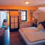 Ein gemütliches Schlafzimmer mit einem Doppelbett mit gelb gestreifter Bettwäsche, einem Kopfteil aus Holz, einem Spitzendach, einer Kommode, einem Fenster mit geblümten Vorhängen und warmer Beleuchtung.