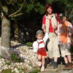 Ein Erwachsener und zwei Kinder gehen gemeinsam im Freien auf einem Steinweg in der Nähe von Bäumen und Felsen.