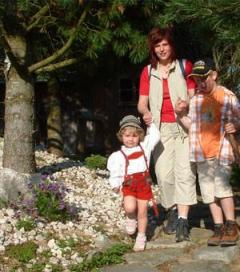 Ein Erwachsener und zwei Kinder gehen gemeinsam im Freien auf einem Steinweg in der Nähe von Bäumen und Felsen.