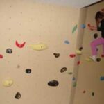 Ein Kind in rosa Hosen klettert an einer Boulderwand mit verschiedenen farbigen Griffen.